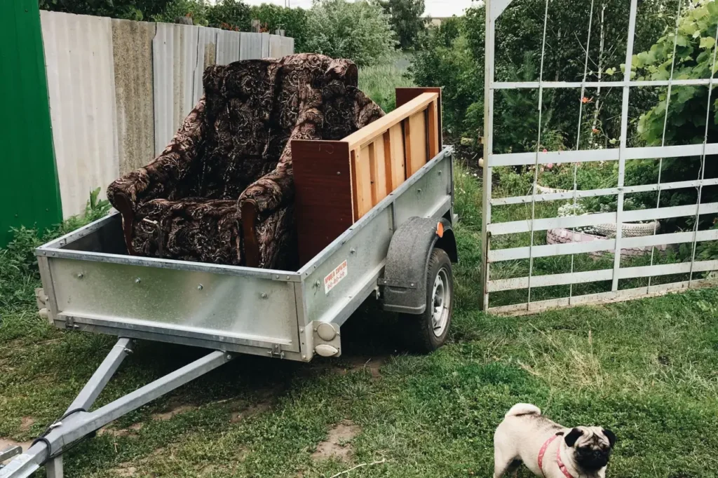 An armchair loaded onto a tipping trailer in a yard